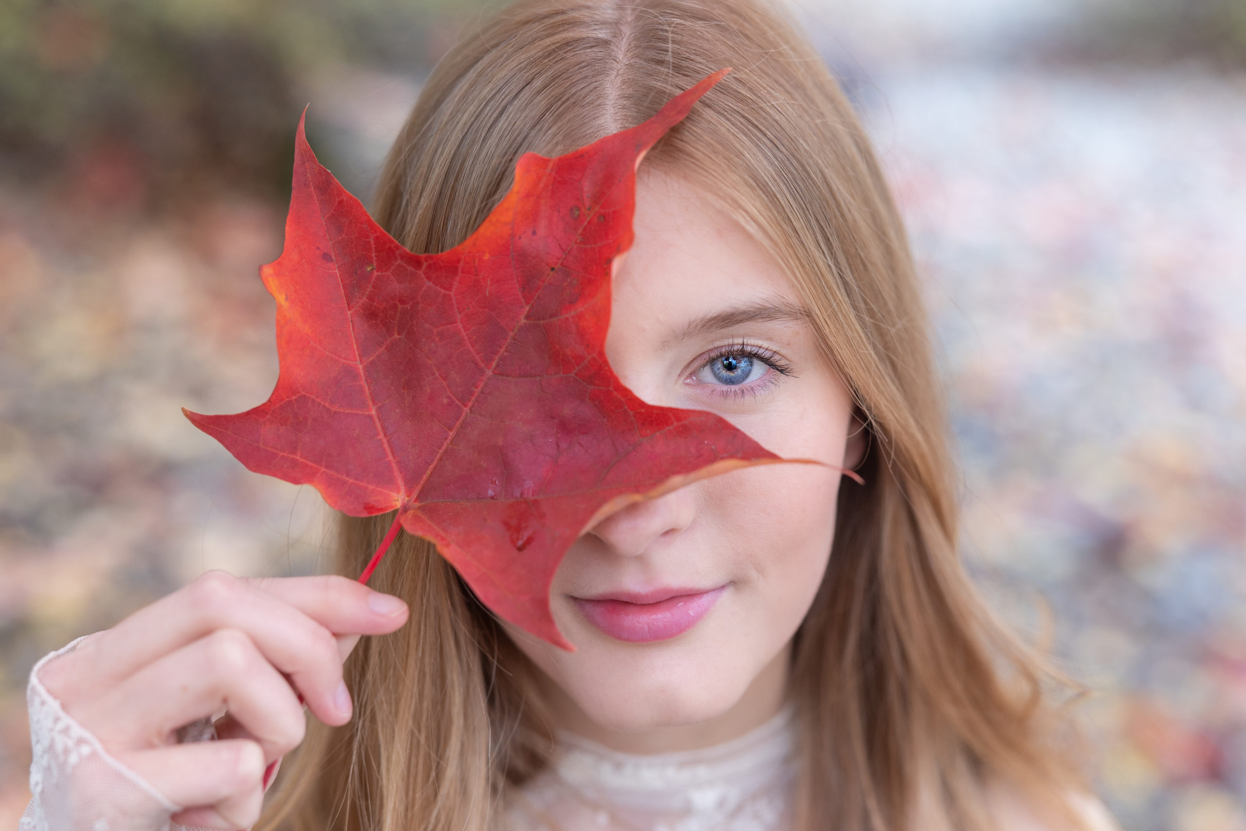 senior holds bright red leaf over one of her eyes
