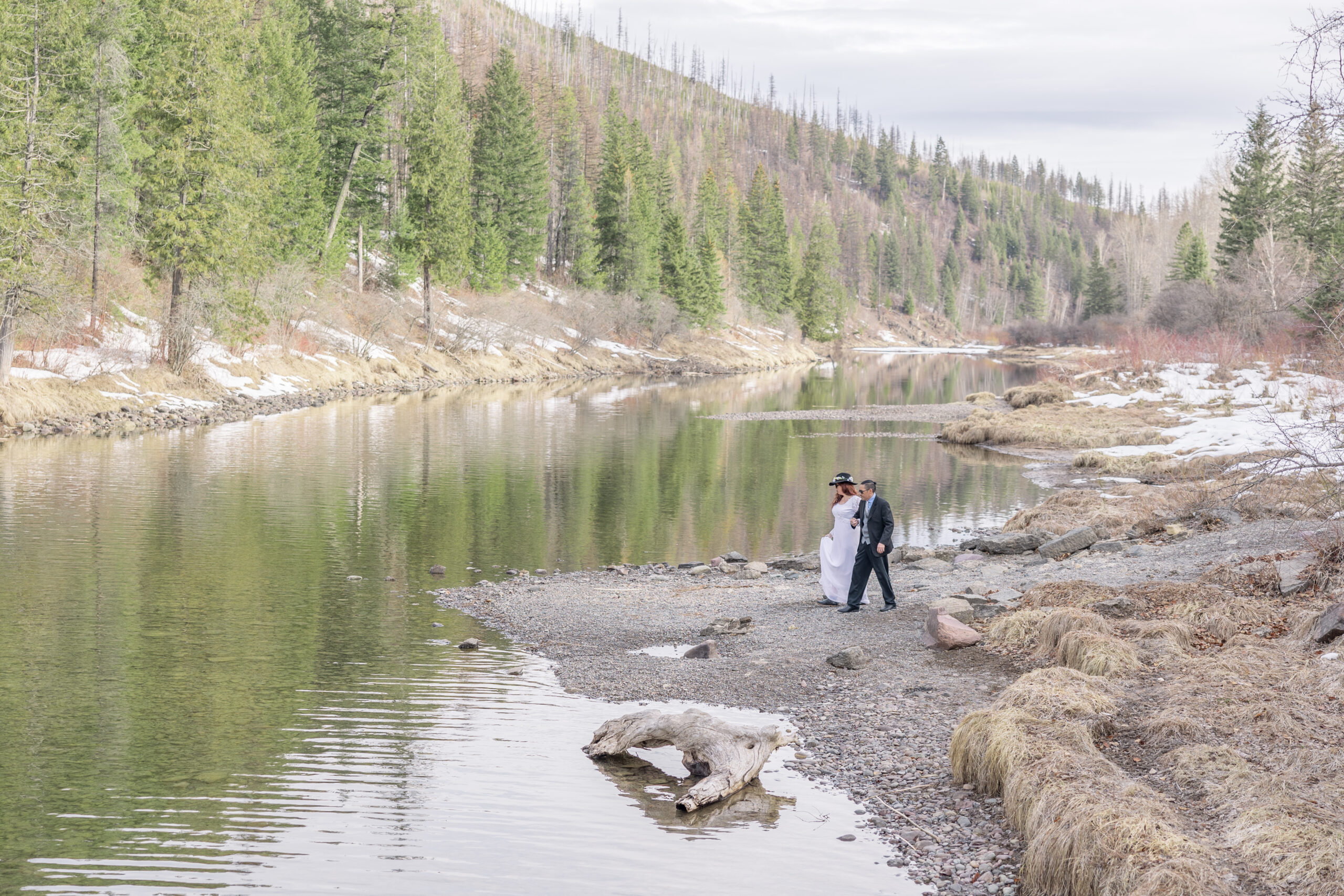 Couple walk along River in Glacier Montana With stunning mountains in the background.